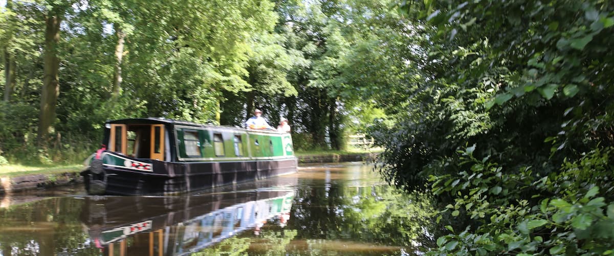 A narrowboat on a calm river surrounded by dense greenery.