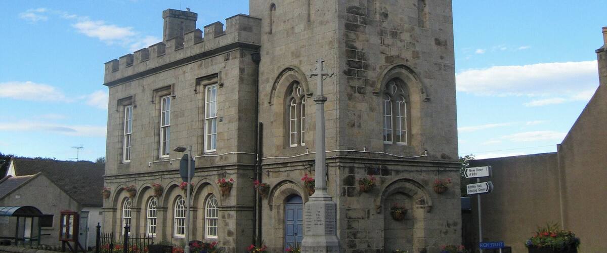A historic stone tower with a pointed spire, arched windows, and a clock.