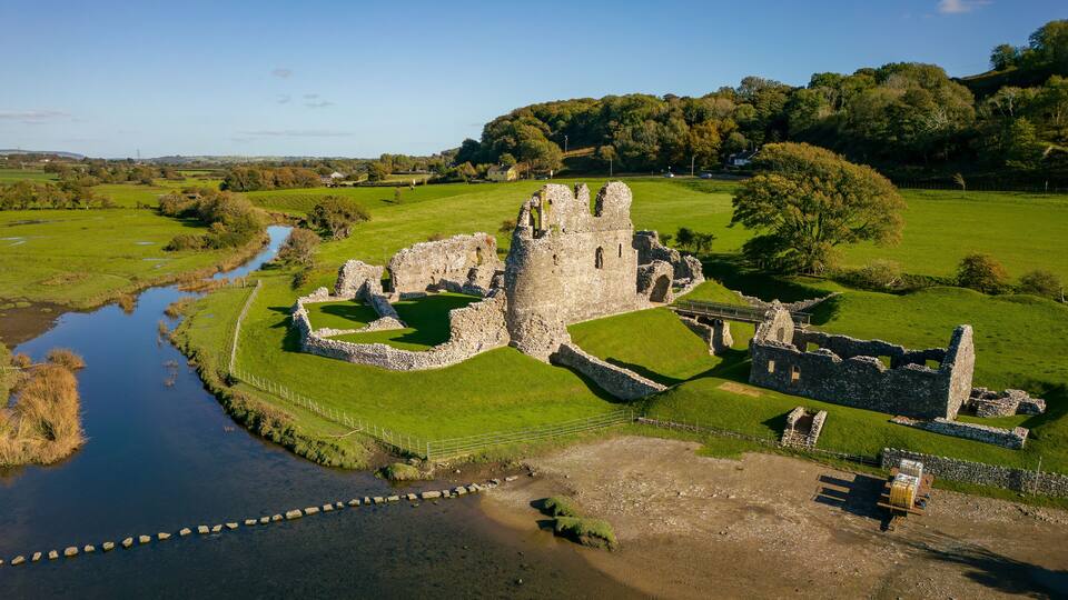 An aerial view of a historic castle ruins surrounded by lush green fields and a river.
