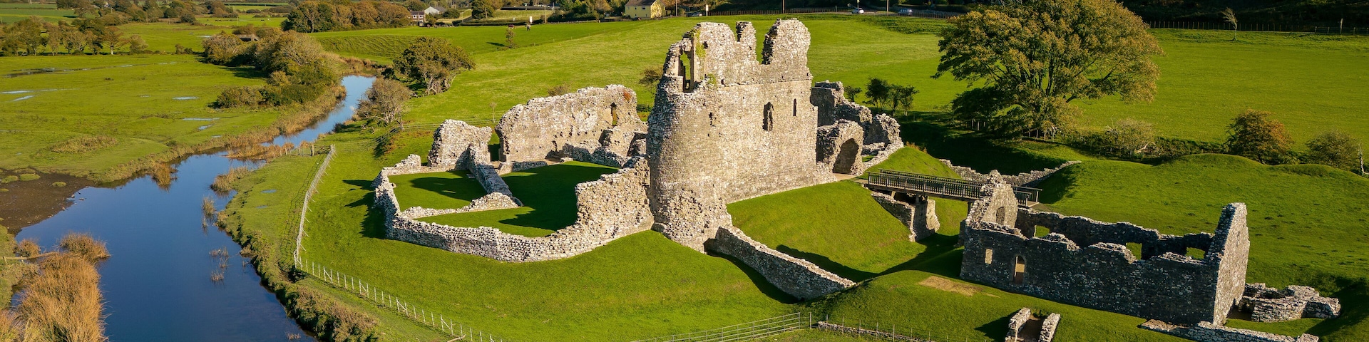 Aerial view of stepping stones crossing a small river leading to an ancient ruined castle (Ogmore, Wales)