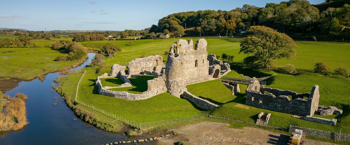 An aerial view of a historic castle ruins surrounded by lush green fields and a river.