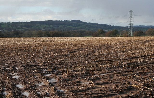 A muddy field with puddles, a power line tower, and rolling hills in the background.