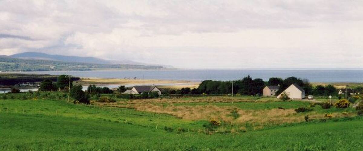 A coastal landscape with houses, green fields, and a body of water.