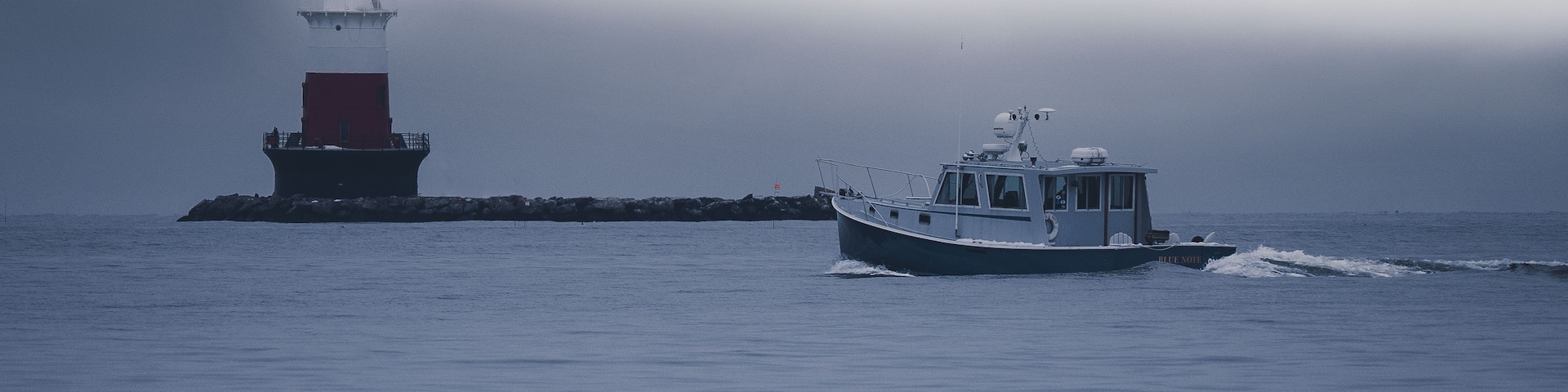 A lighthouse and a boat on calm waters under a cloudy sky.