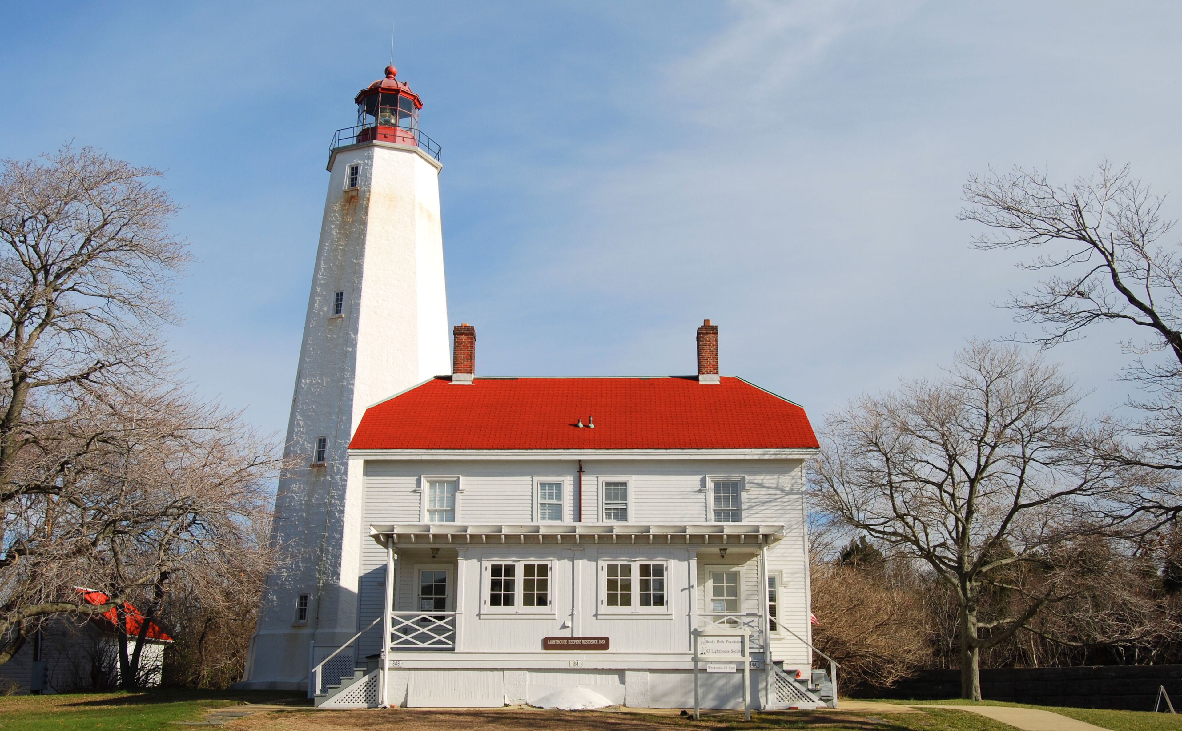 A white lighthouse with a red roof and a white building with a red roof in front of it.
