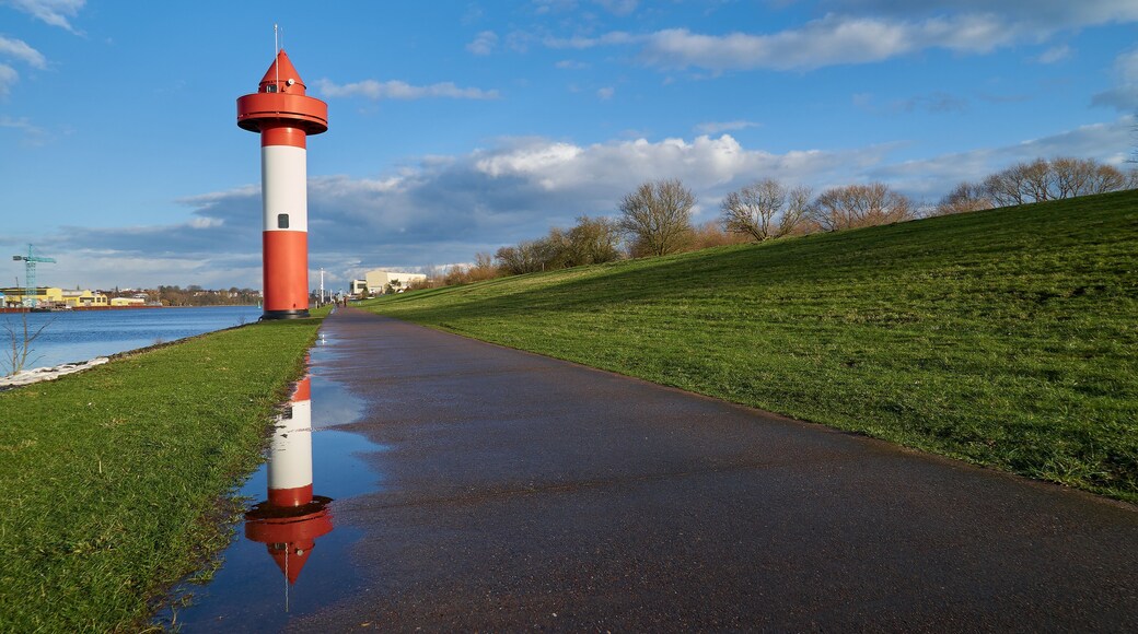 small lighthouse at Ritzenbütteler Sand, municipality Lemwerder (district Wesermarsch, Germany) on a sunny spring day with vivid blue sky and clouds reflecting in a puddle on the footpath next to dike