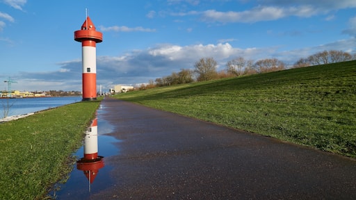 small lighthouse at Ritzenbütteler Sand, municipality Lemwerder (district Wesermarsch, Germany) on a sunny spring day with vivid blue sky and clouds reflecting in a puddle on the footpath next to dike