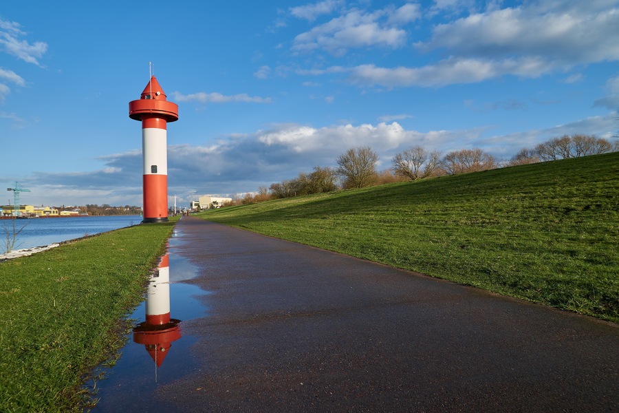 small lighthouse at Ritzenbütteler Sand, municipality Lemwerder (district Wesermarsch, Germany) on a sunny spring day with vivid blue sky and clouds reflecting in a puddle on the footpath next to dike