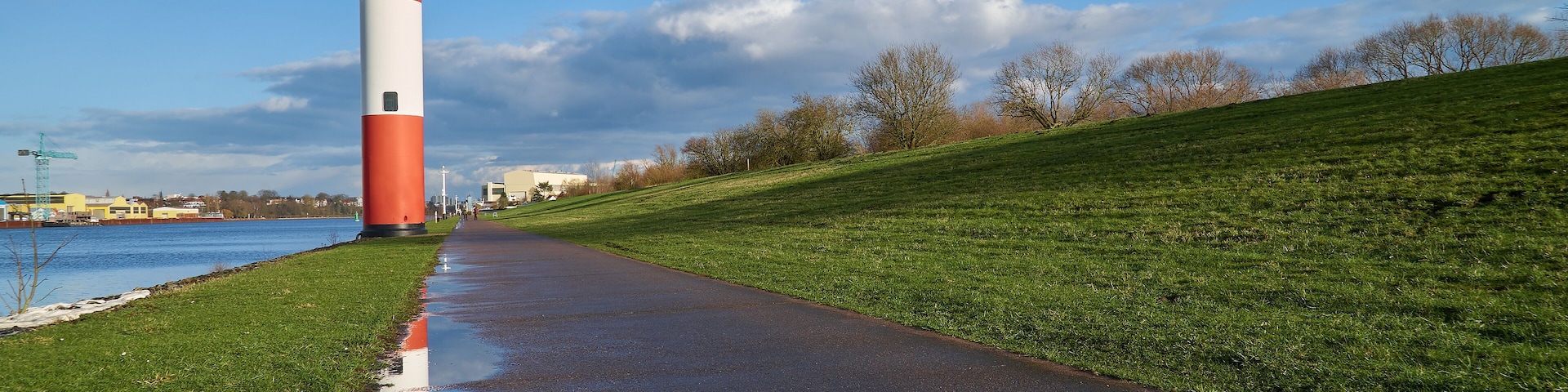small lighthouse at Ritzenbütteler Sand, municipality Lemwerder (district Wesermarsch, Germany) on a sunny spring day with vivid blue sky and clouds reflecting in a puddle on the footpath next to dike