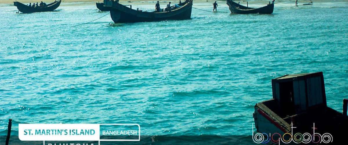 Boats on a turquoise sea with a sandy beach and dense greenery in the background.
