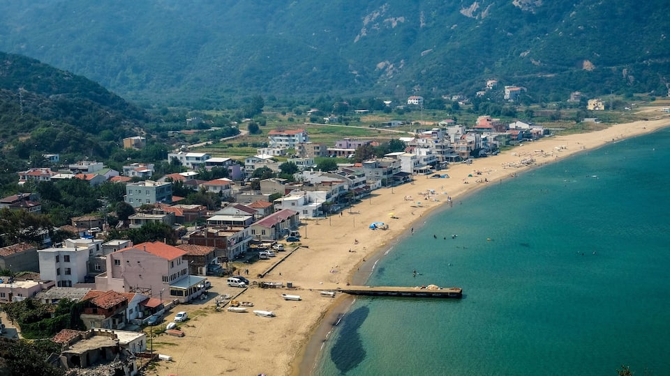 A coastal town with a beach, buildings, and mountains in the background.