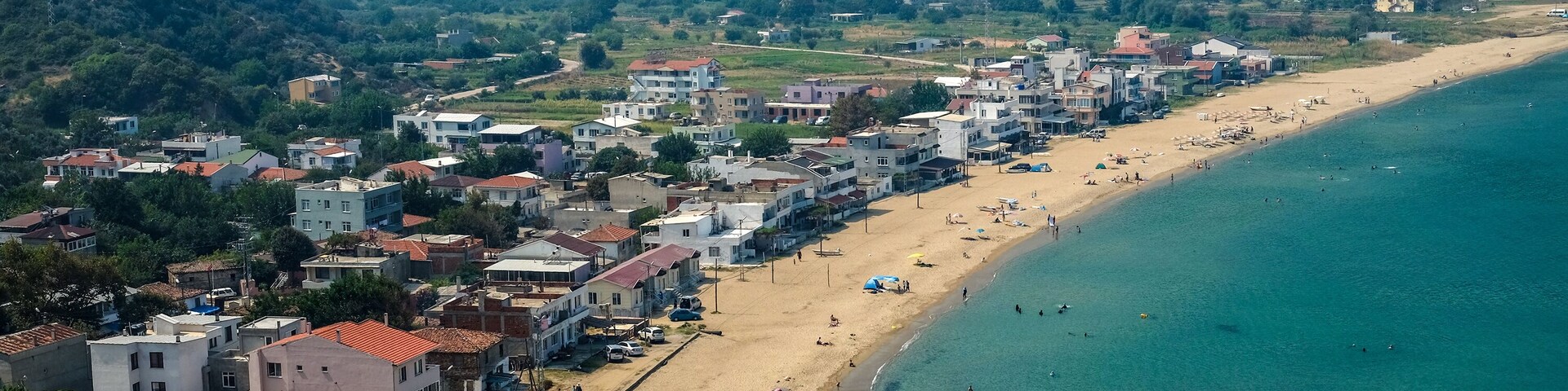 Un pueblo costero con playa, edificios y montañas al fondo.