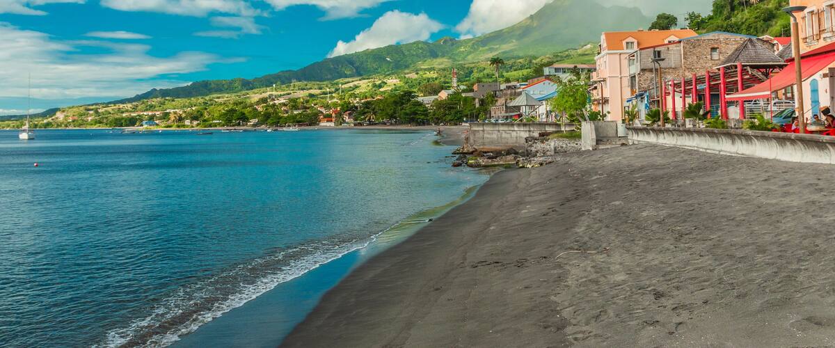 A beach with a clear blue sea, a sandy shore, and colorful buildings along the coastline.