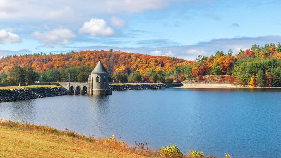 A tranquil lake with a stone tower, surrounded by autumn-colored trees and a clear sky.