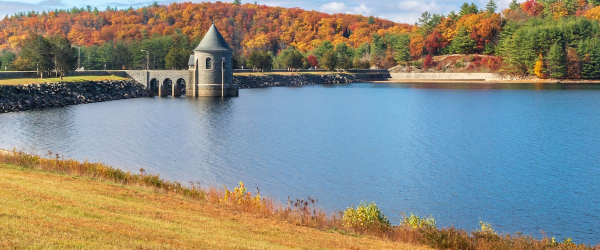 A tranquil lake with a stone tower, surrounded by autumn-colored trees and a clear sky.