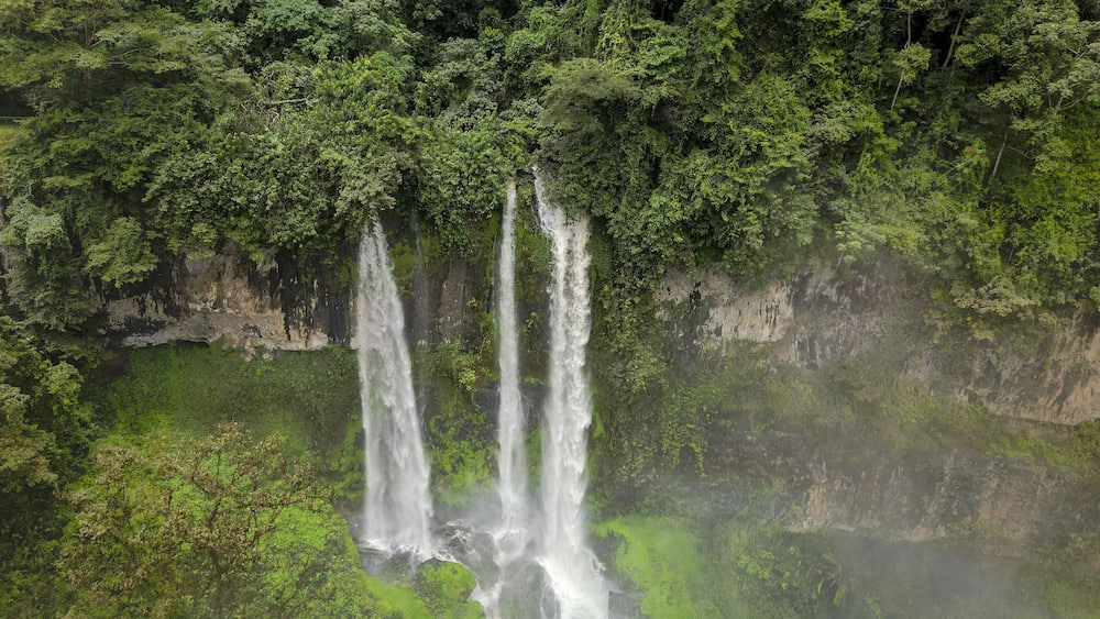 Aerial view of cascading water plummeting down the cliffside into a misty pool below, surrounded by dense green foliage, Nkongsamba, Littoral Region, Cameroon.