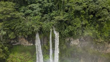 A waterfall cascading down a lush, green cliff surrounded by dense forest.