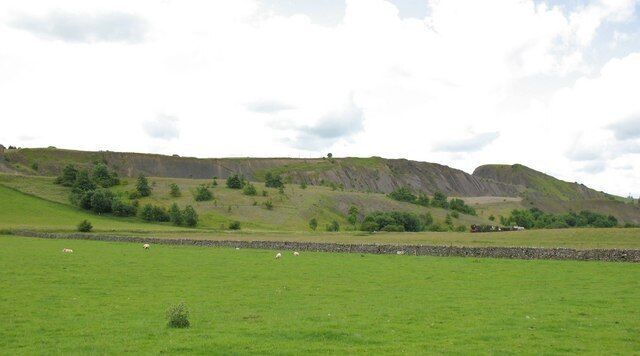 A green field with sheep, rolling hills, and a stone wall.