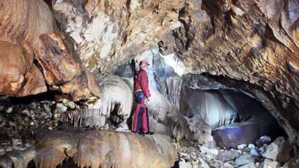 A cave with stalactites, stalagmites, and a person in a red outfit.