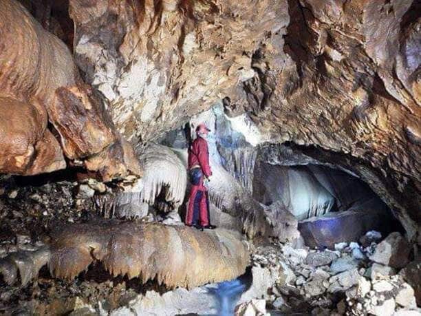 A cave with stalactites, stalagmites, and a person in a red outfit.