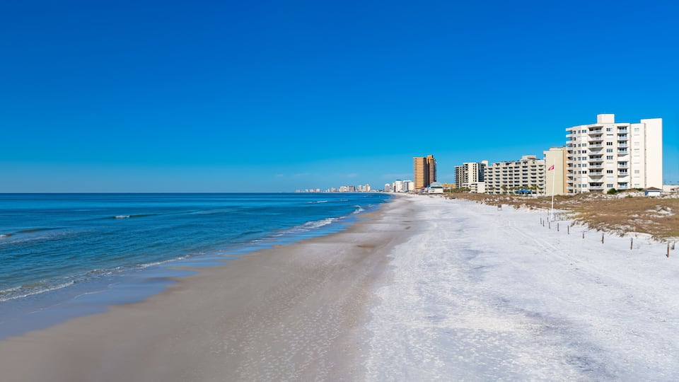 A beach with a clear blue sky, sandy shore, and tall buildings in the background.