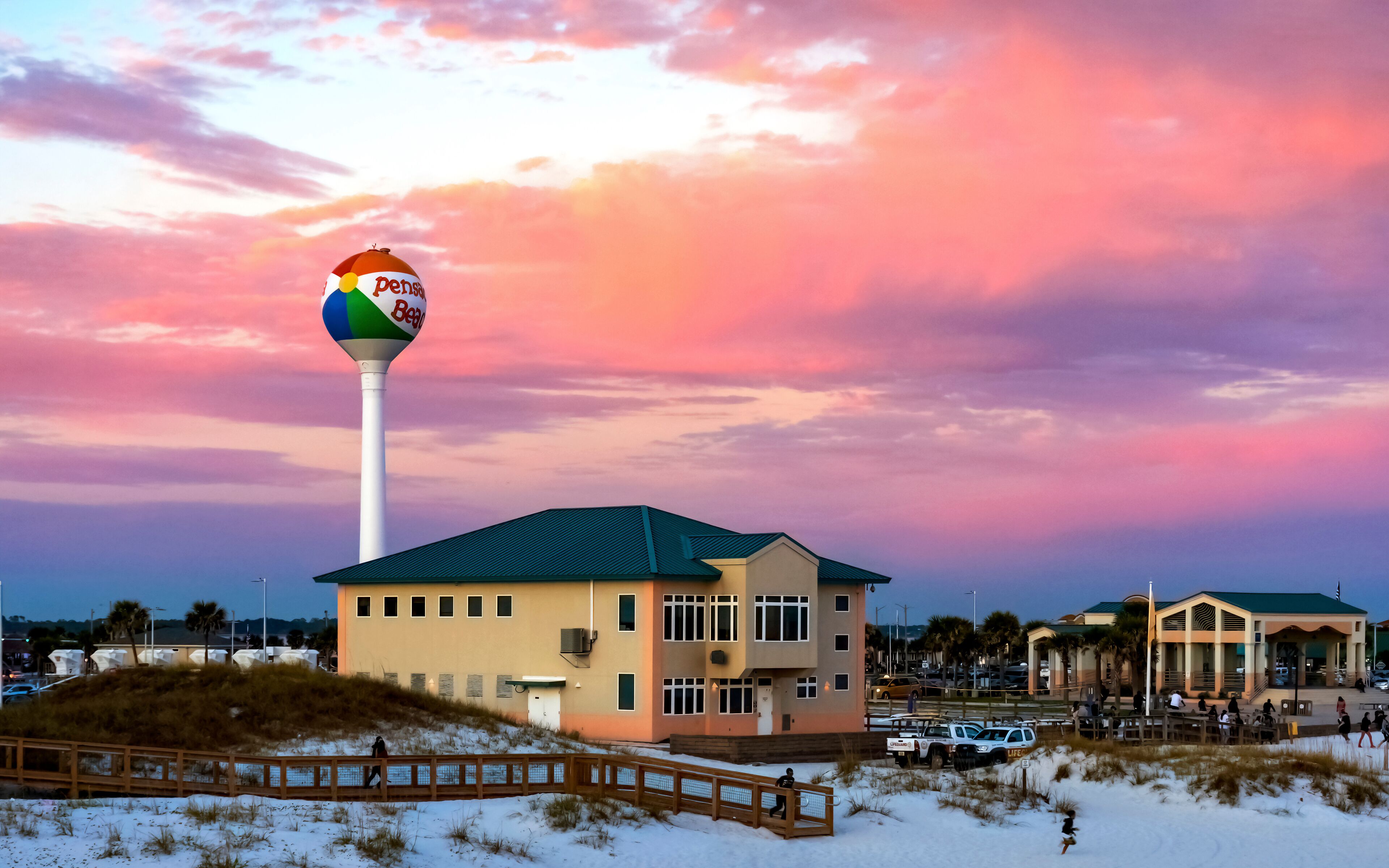 A beach house with a colorful beach ball on a pole, a wooden boardwalk, and a sunset sky.