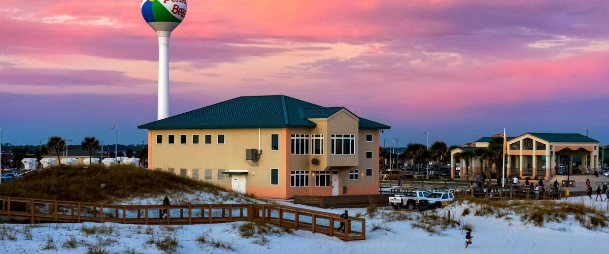 A beach house with a colorful beach ball on a pole, a wooden boardwalk, and a sunset sky.