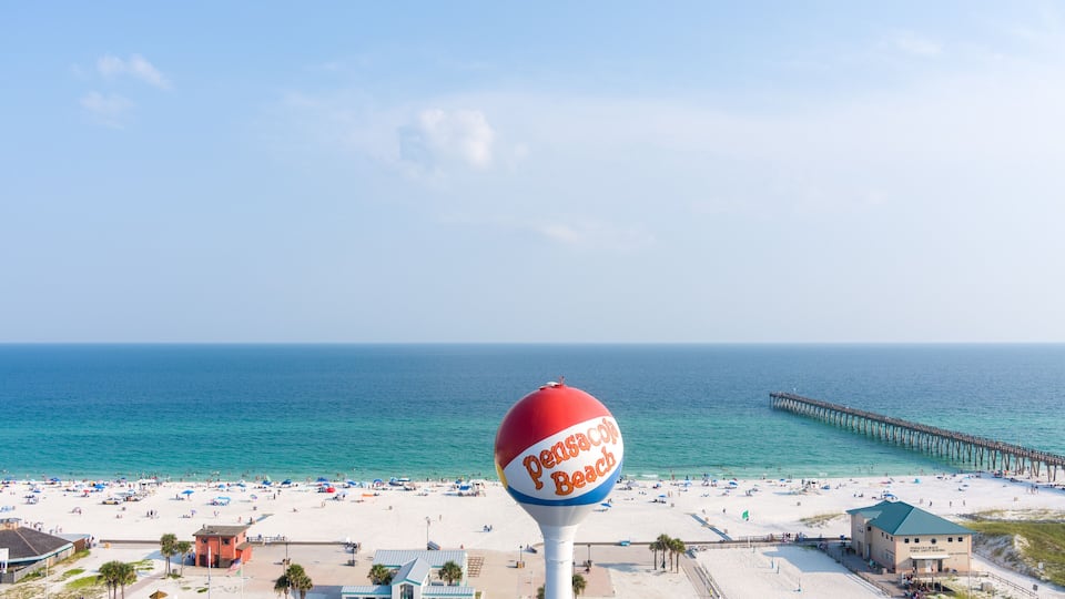 A beach with a pier, a water tower, and beachgoers.