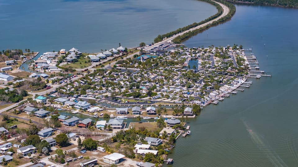 An aerial view of a coastal community with a marina, houses, and a curved road along the water.