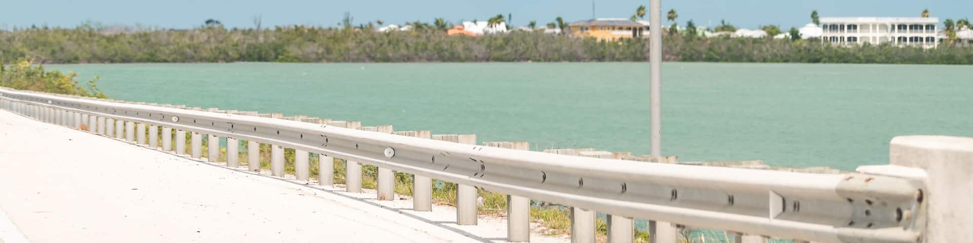 A sign reading "CUDJOE KEY" by a coastal road with a clear sky and calm sea.