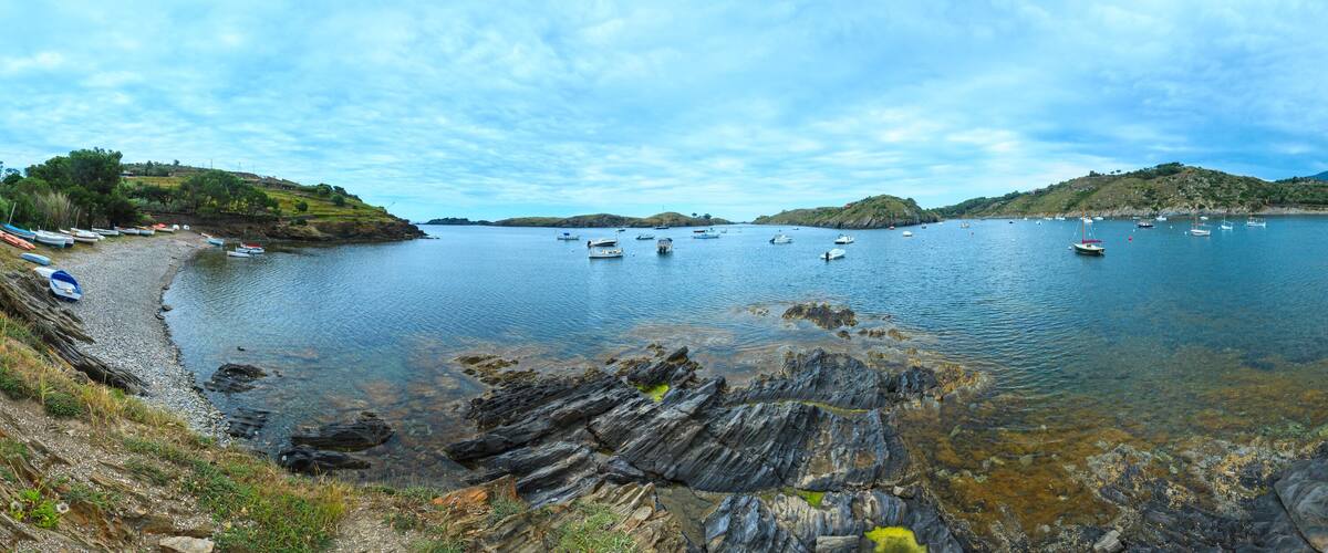A coastal bay with boats, rocky shoreline, and distant hills.