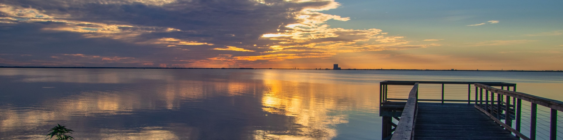 Un muelle de madera se adentra en aguas tranquilas, reflejando el cielo y las nubes.
