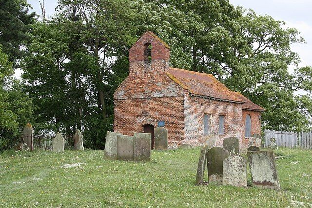 An old brick church with a bell tower, surrounded by gravestones in a grassy field.