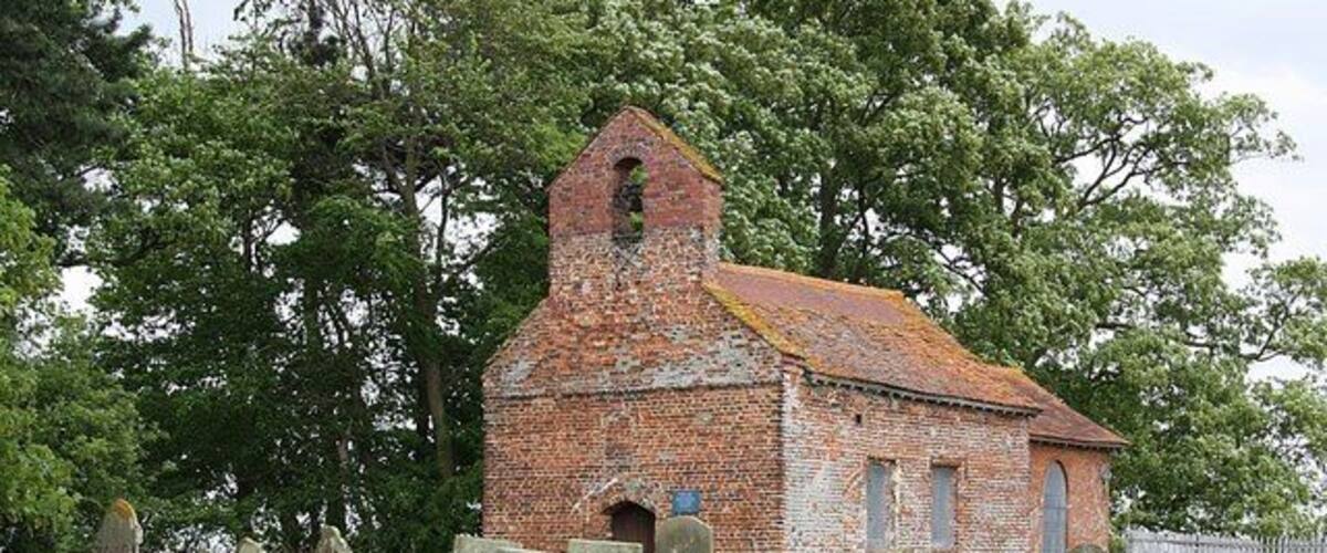 An old brick church with a bell tower, surrounded by gravestones in a grassy field.
