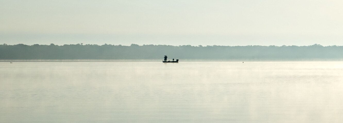 Un lago tranquilo con un barco pequeño y una persona a lo lejos.