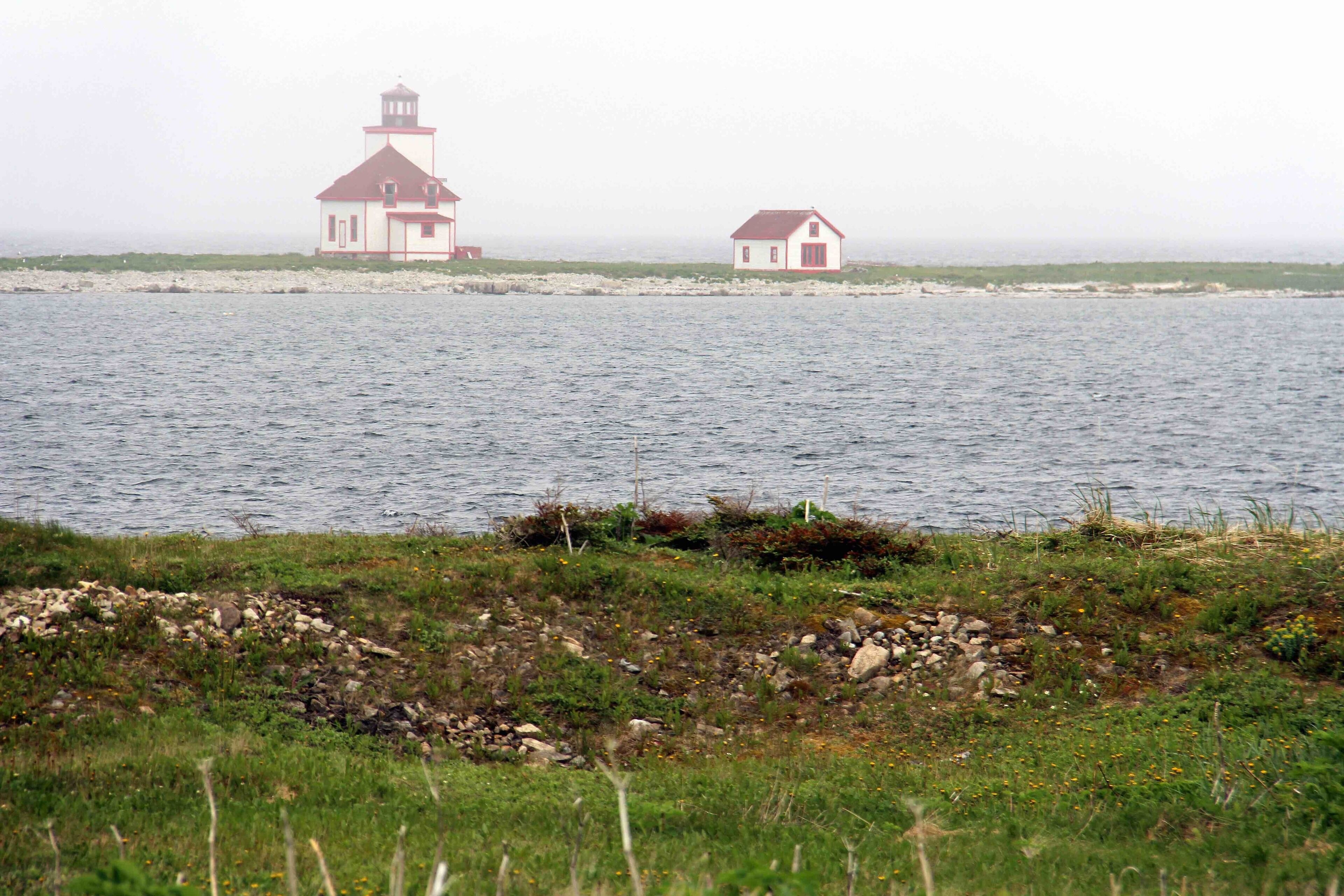 A lighthouse and a small house by the water.
