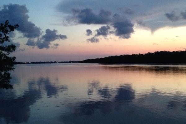Um lago calmo ao entardecer, com o perfil de árvores e uma linha de costa distante.