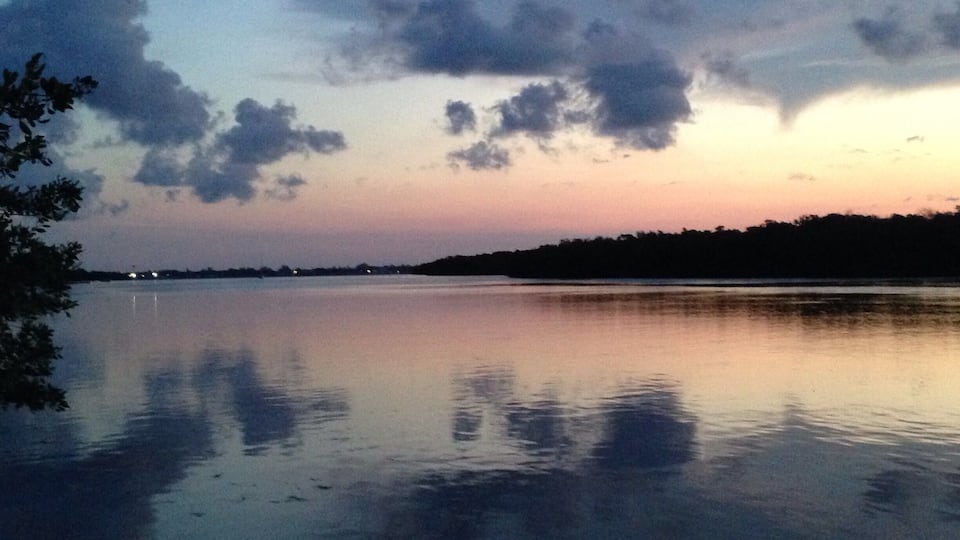 A calm lake at dusk with a silhouette of trees and a distant shoreline.