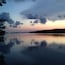 Un lac paisible au crépuscule, avec la silhouette d’arbres et une rive lointaine.