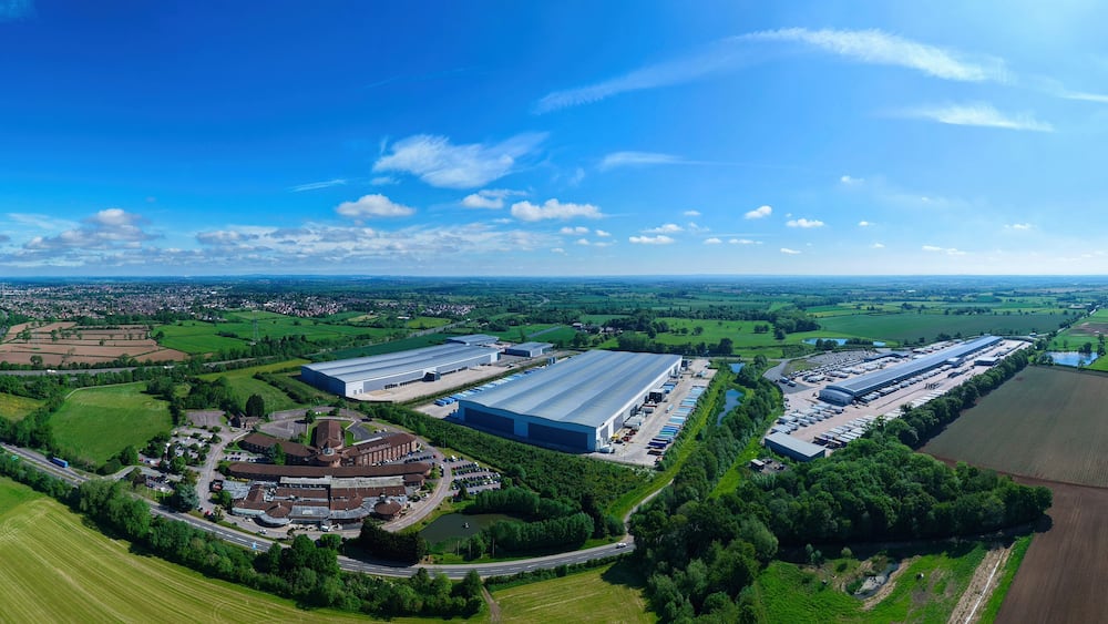 Aerial view of large industrial warehouses and distribution centers surrounded by green fields and rural landscape under a clear blue sky Hinckley, England, United Kingdom.