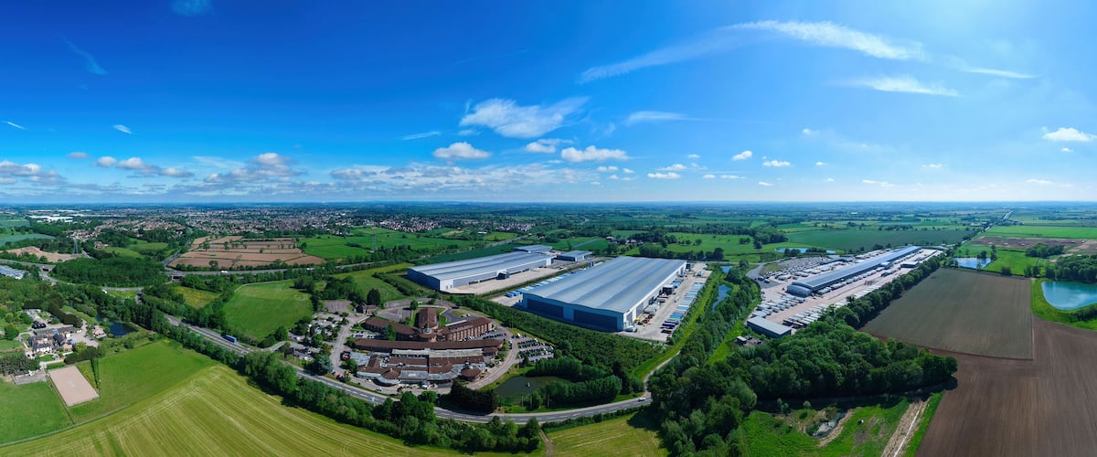Aerial view of large industrial warehouses and distribution centers surrounded by green fields and rural landscape under a clear blue sky Hinckley, England, United Kingdom.