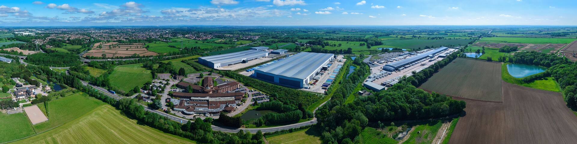 An aerial view of a large industrial area with multiple warehouses, surrounded by green fields and a small lake.