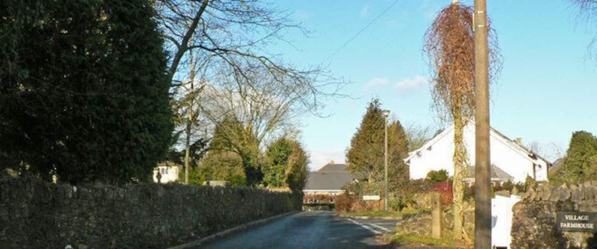 A rural road with a stone wall on one side and a white house with a sign reading "VILLAGE FARMHOUSE" on the other.