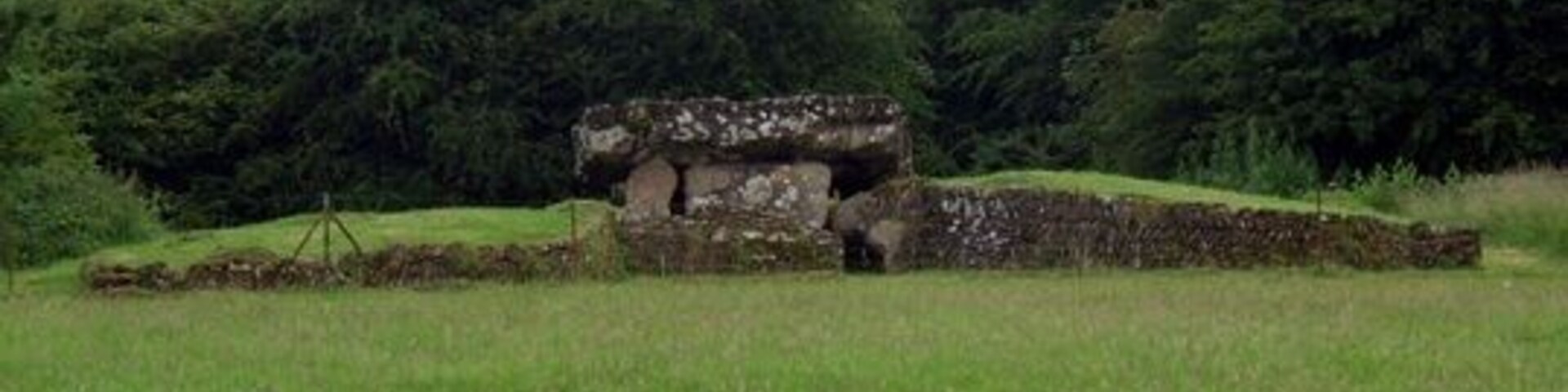 Uma construção de pedra em um campo gramado, com árvores ao fundo.