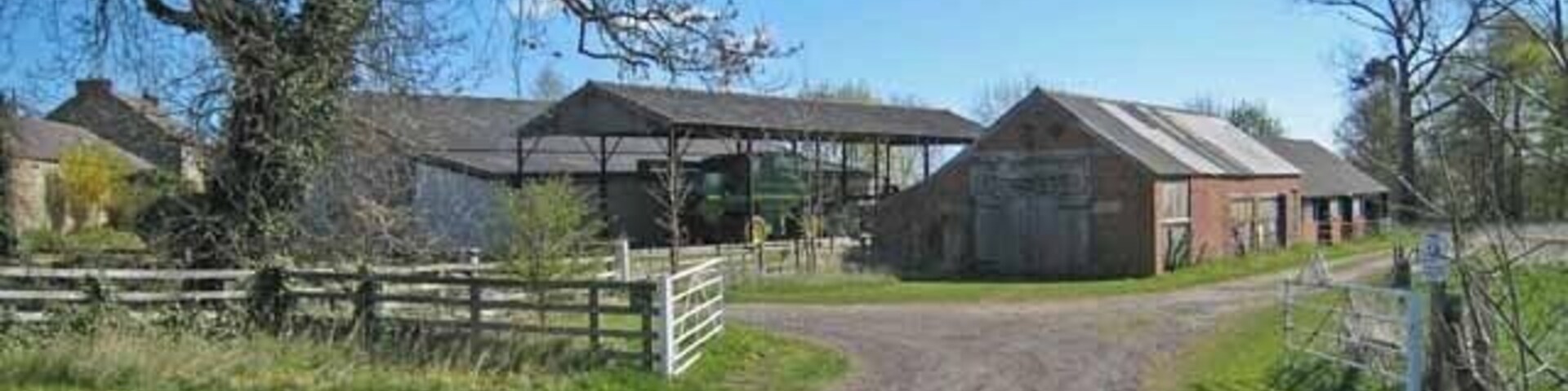 A gravel road leading to a farm with barns and a fenced area.
