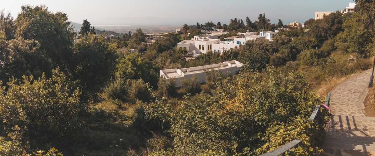 A hillside with white buildings, a clear blue sky, and a distant view of the sea.