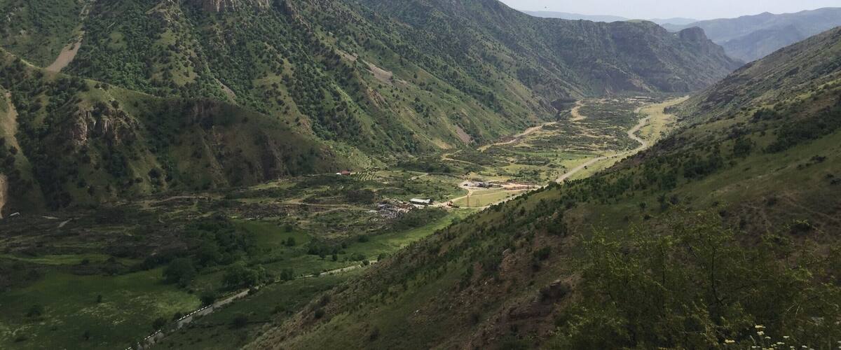 A mountainous landscape with a valley, a river, and scattered buildings.