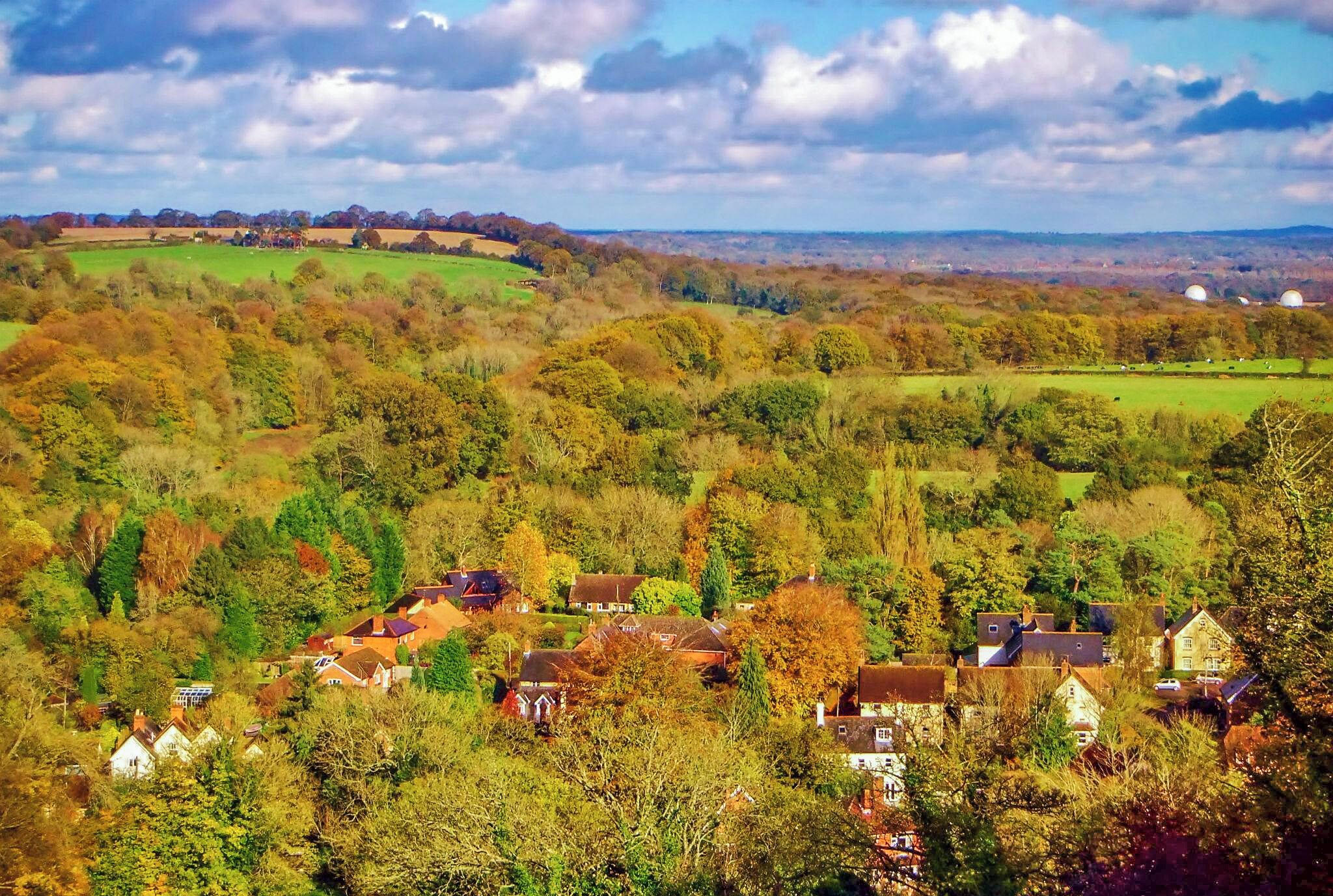 A rural landscape with rolling hills, scattered houses, and a mix of deciduous trees.