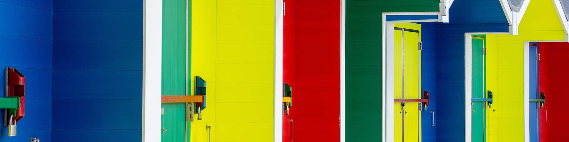 A row of brightly colored beach huts with doors and windows.