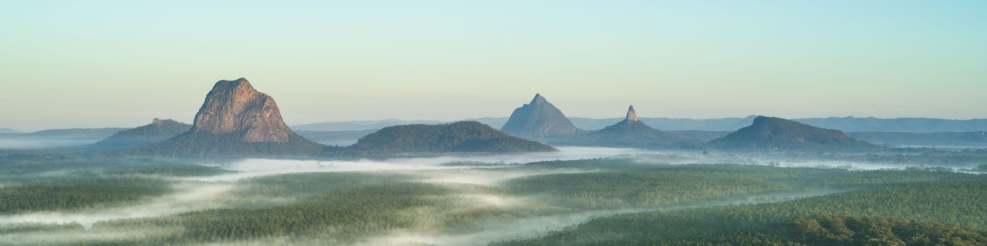 Paisagem arborizada com três montanhas imponentes e céu claro.